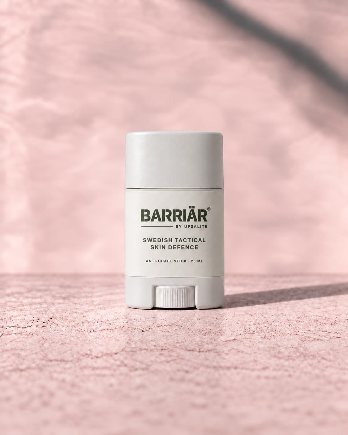 Barriär Anti-Chafe Stick, a short 25 ml white twist-up stick with a white wrap-around label printed in olive with the Barriär by Upsalite wordmark, Swedish Tactical Skin Defence and Anti-Chafe Stick 25 ml, standing on pale concrete against a plaster wall