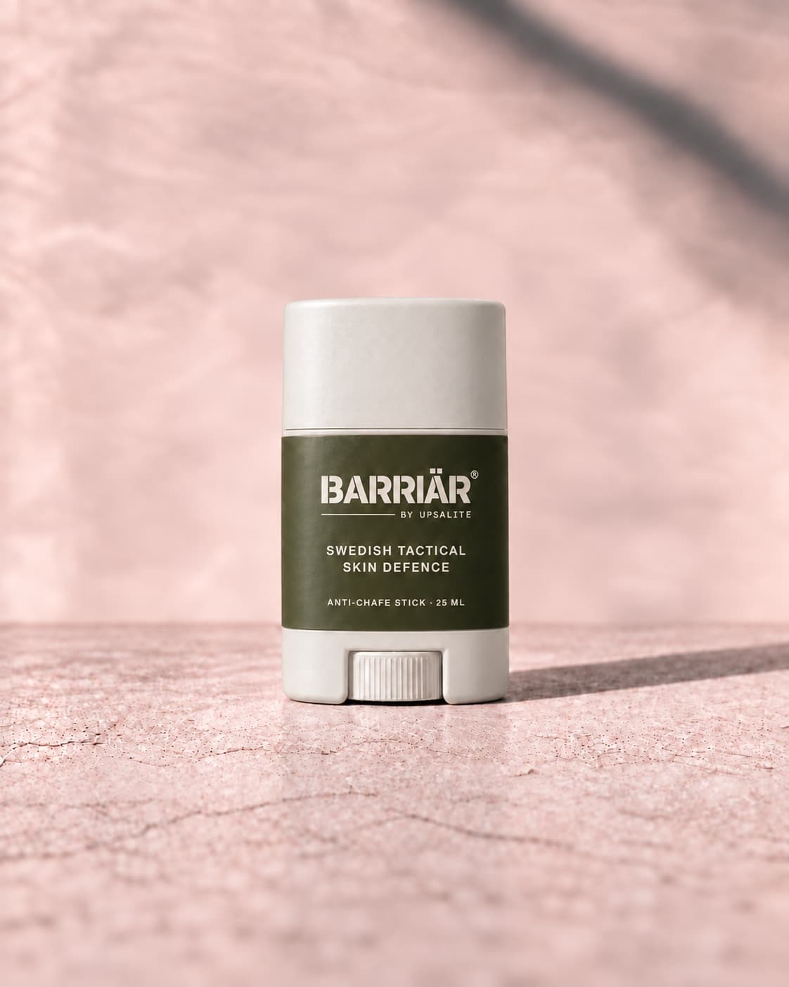 Barriär Anti-Chafe Stick, a short 25 ml white twist-up stick with an olive wrap-around label printed in white with the Barriär by Upsalite wordmark, Swedish Tactical Skin Defence and Anti-Chafe Stick 25 ml, standing on pale concrete against a plaster wall