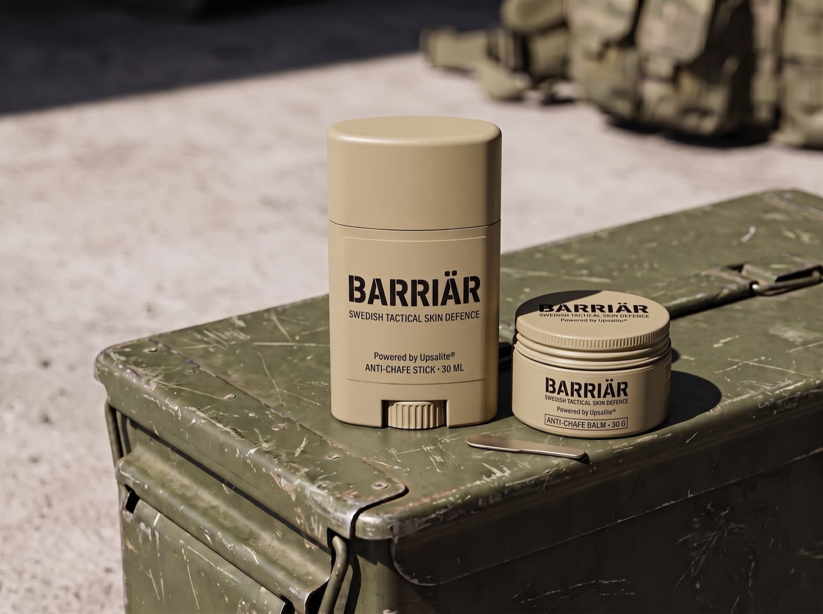 Barriär anti-chafe stick and jar in matte sand-beige packaging on a scratched olive-green ammunition box in hard sunlight, both printed with the Barriär wordmark in Barlow condensed over Swedish Tactical Skin Defence