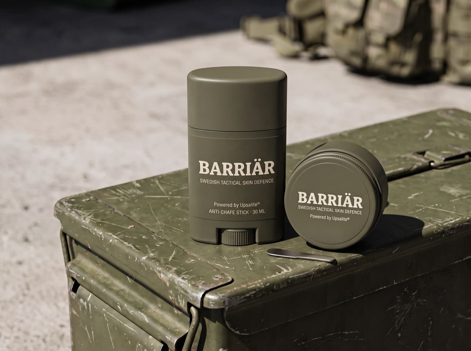 Barriär anti-chafe stick and jar in matte olive packaging on a scratched olive-green ammunition box in hard sunlight, both printed with the Barriär wordmark in Bitter slab-serif over Swedish Tactical Skin Defence