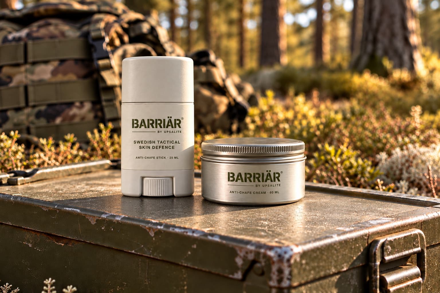 Barriär Anti-Chafe Stick 25 ml, a white stick with a white label, and the wider, lower Anti-Chafe Cream 60 ml aluminium tin with a clear sticker, both printed in olive with the Barriär by Upsalite wordmark, on a worn olive ammunition box in a sunlit pine forest with a camouflage rucksack behind